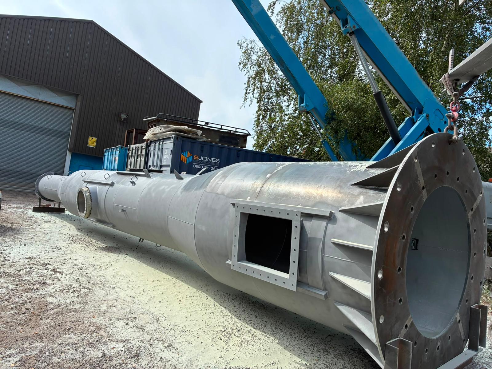 Large steel chimney section during shot blasting preparation — access opening and reinforced flange
